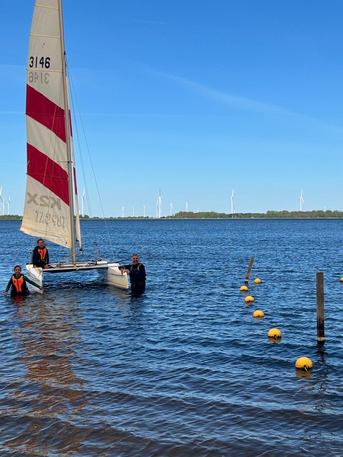 Een zeilboot op het water met mensen in het water ernaast